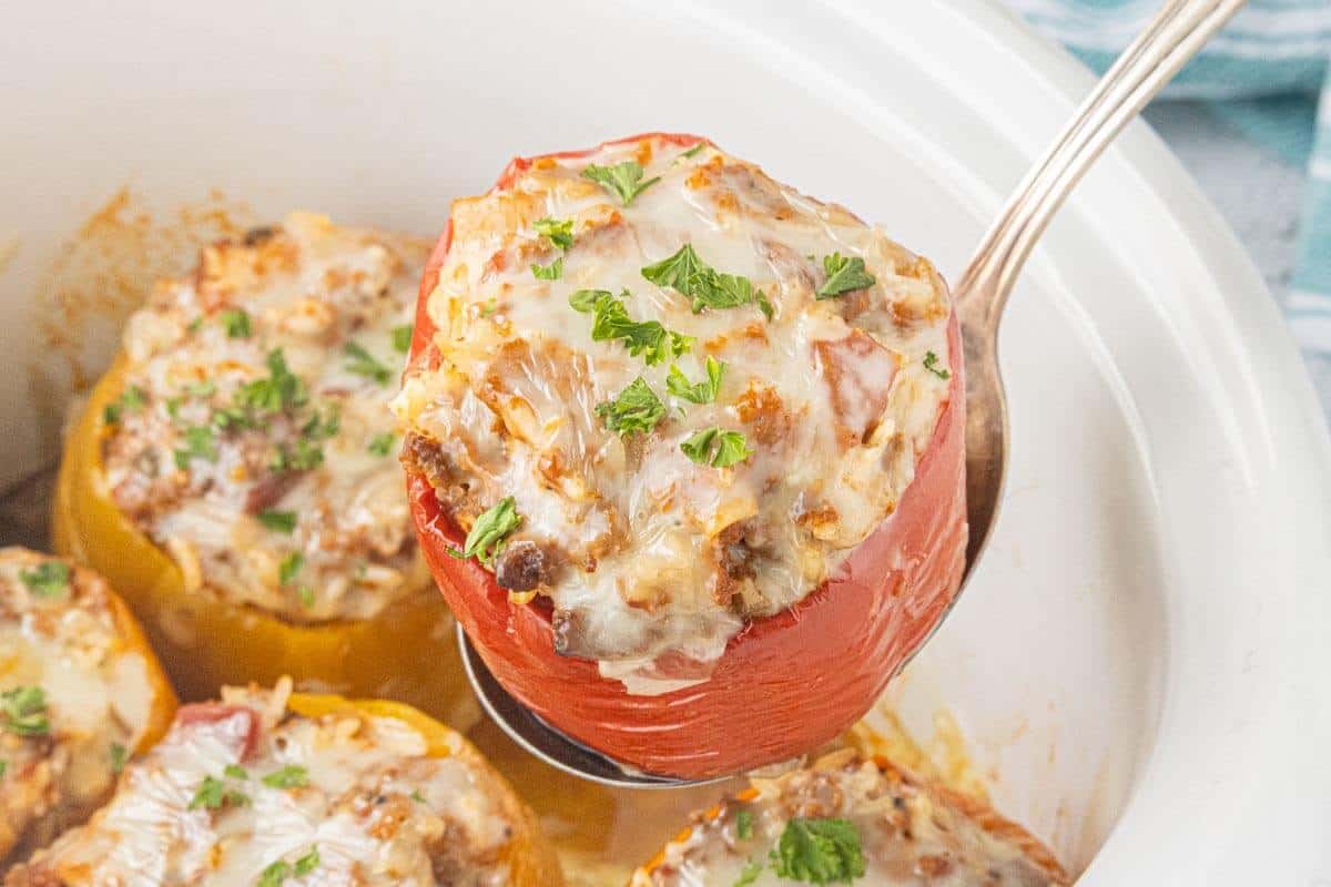 Red stuffed bell pepper topped with melted mozzarella cheese and fresh parsley, being lifted from the slow cooker with a serving spoon.