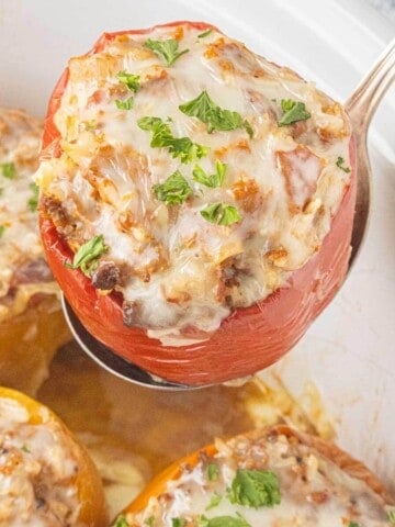Close-up of a Stuffed Bell Pepper being lifted from the crockpot with a serving spoon. The peppers are filled with seasoned ground beef, rice, and sauce.