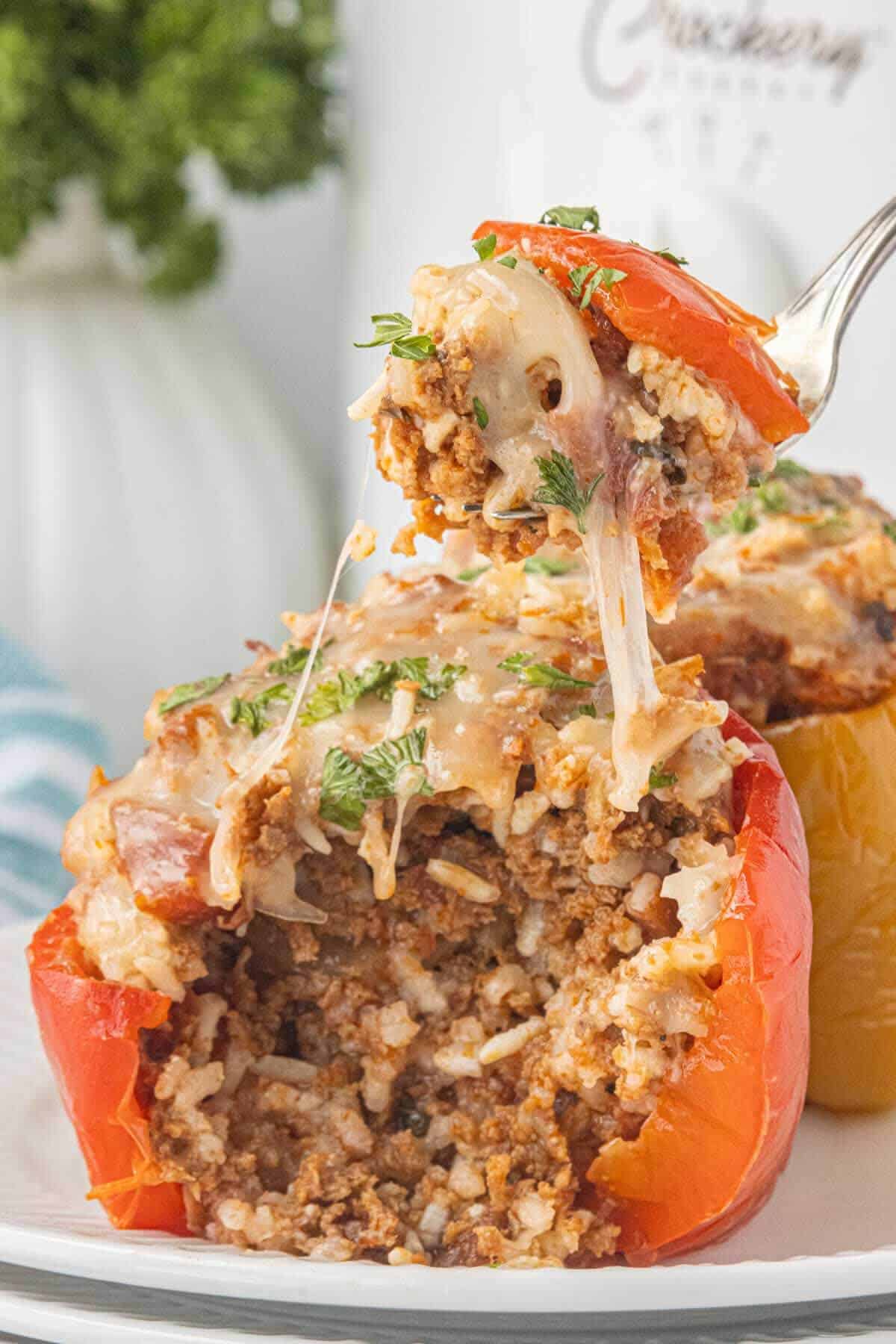 Cooked stuffed bell pepper on a plate. The pepper has been cut in half and a fork is lifting a cheesy bite from the center.