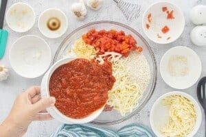 Pasta sauce being poured into a glass mixing bowl with ground beef, uncooked rice, diced tomatoes, onion, garlic, and shredded mozzarella for crockpot stuffed bell peppers.
