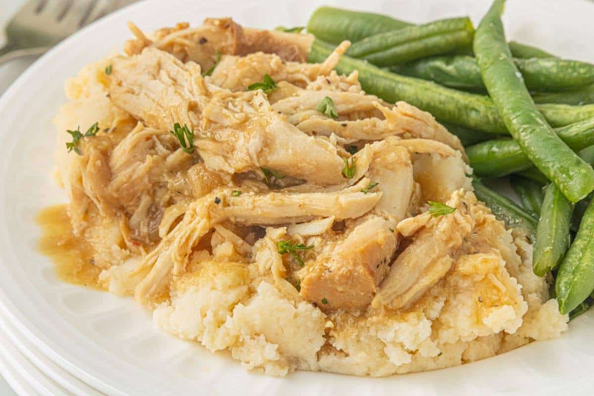 Slow cooker turkey and gravy served over mashed potatoes with fresh green beans on the side.