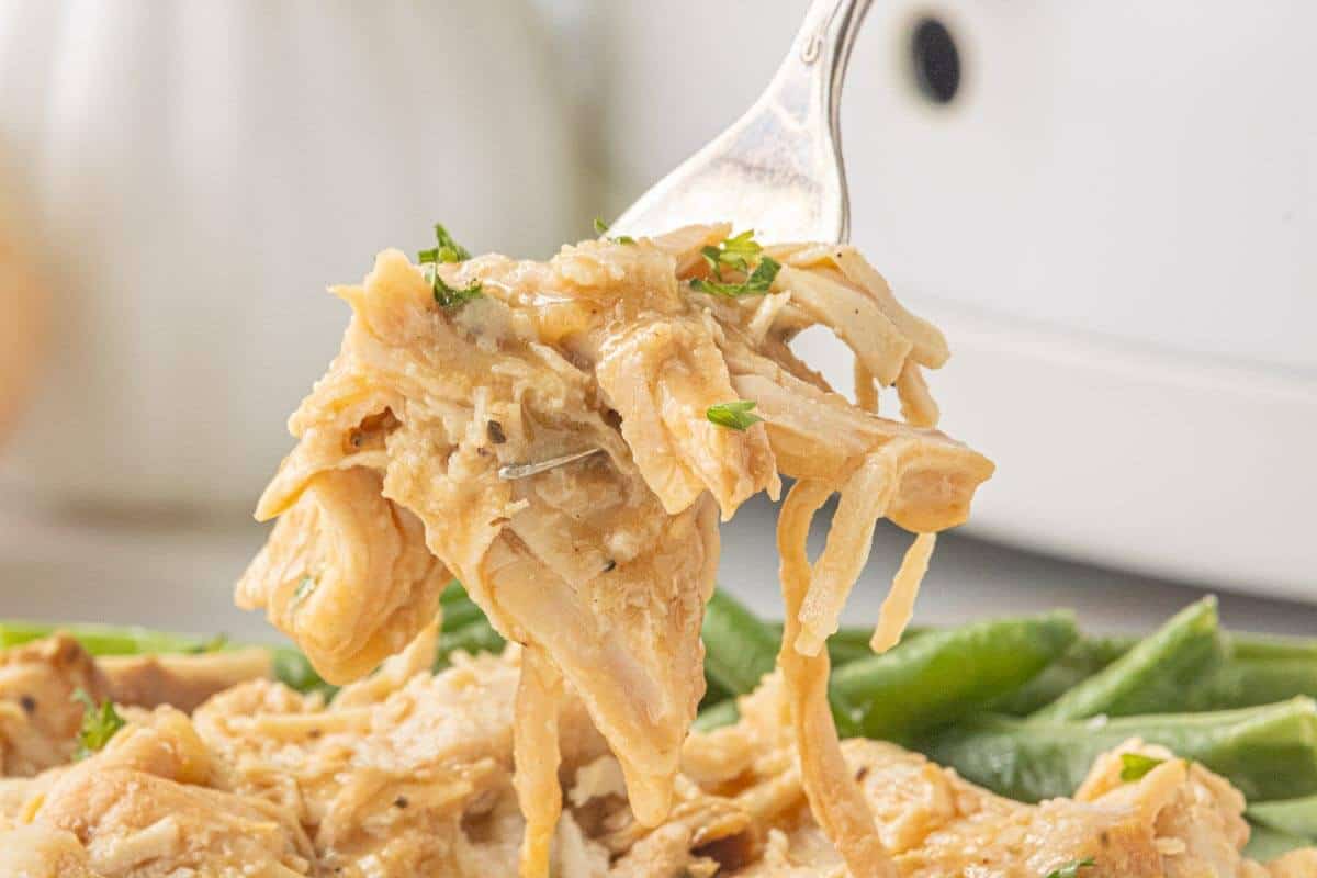 Shredded turkey on a fork above a plate of mashed potatoes and green beans.