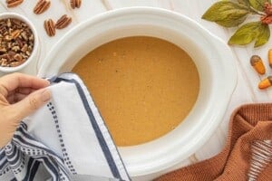 A striped kitchen towel being positioned over the rim of a crockpot filled with pumpkin pudding batter.