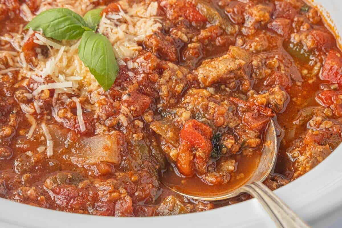 Close-up of chunky homemade Crockpot Spaghetti Sauce with tomatoes, bell peppers, and Italian sausage, topped with grated Parmesan cheese and fresh basil.